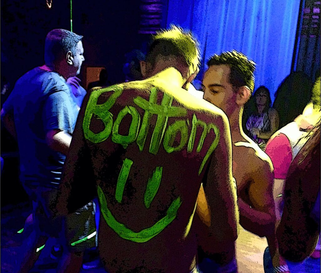 Shirtless man with neon painted word Bottom on his back at Pride party.