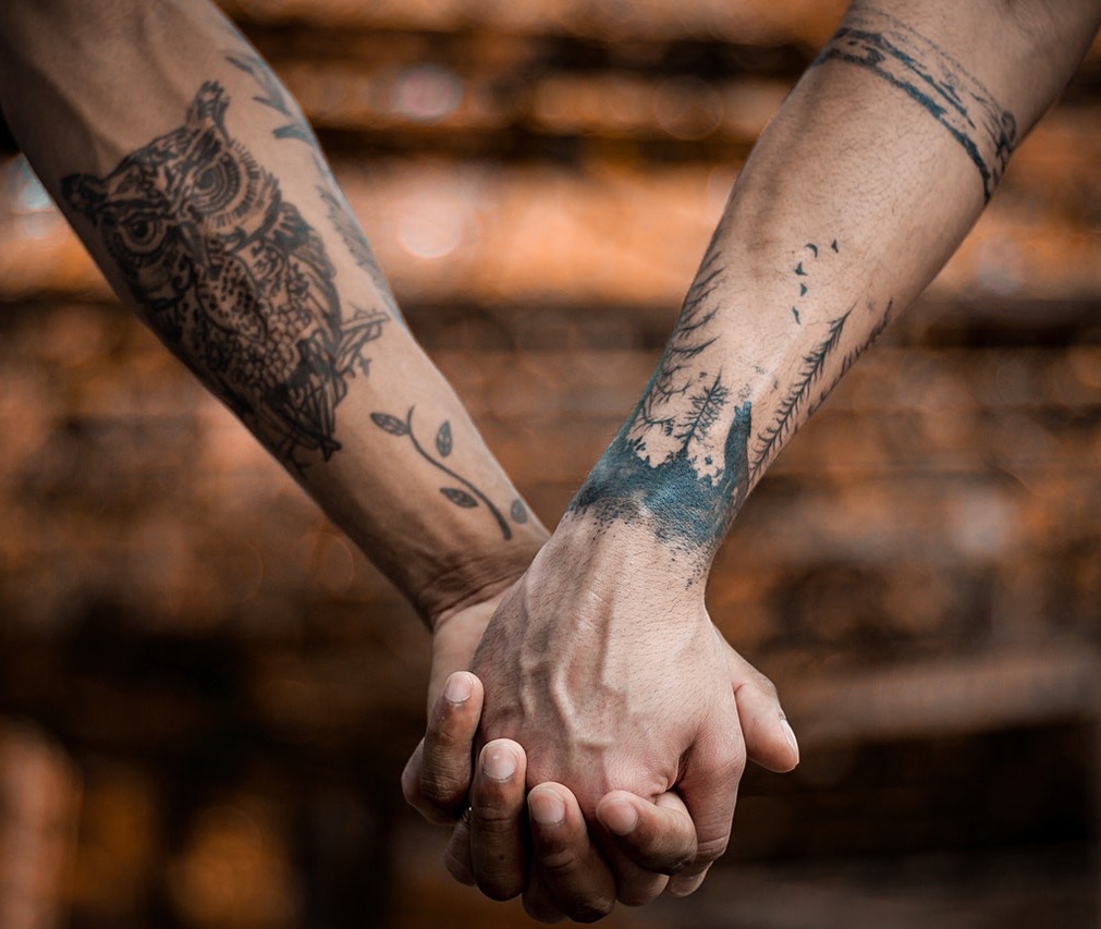 Gay couple's tattoo arms holding hands