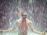 Young man under pouring waterfall