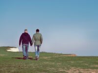 Gay men couple holding hands walking above white cliffs