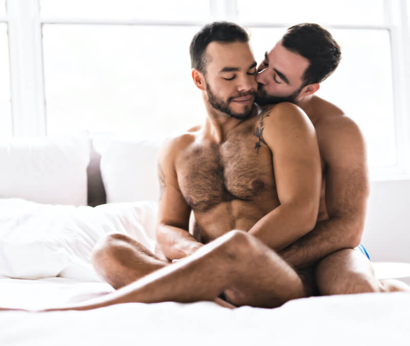 Naked gay couple hugging in bed