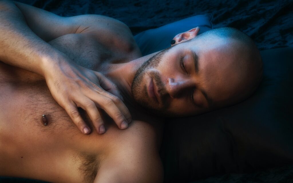Shirtless bearded man lying down with eyes closed