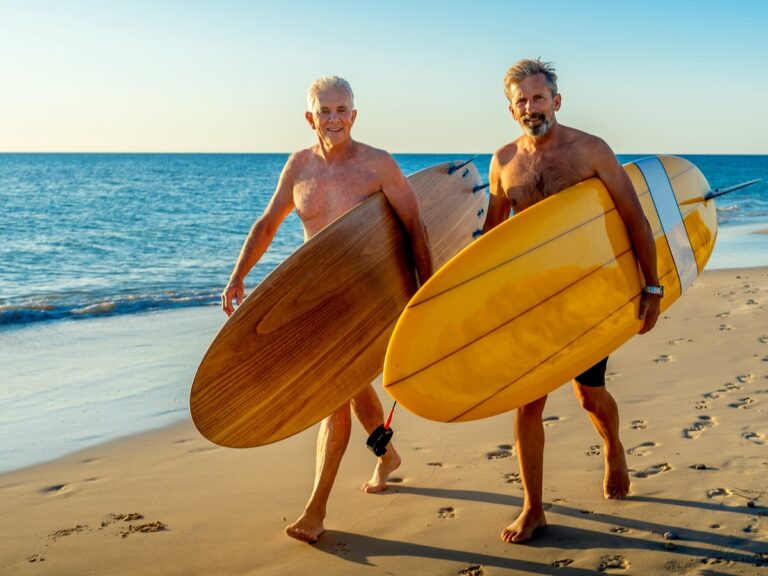 Two mature gay men carrying surfboards